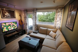 A living room with a sofa, a coffee table, a television, a guitar, and a balcony with curtains. - Cozy two-story apartment with a sauna (Tromsø)