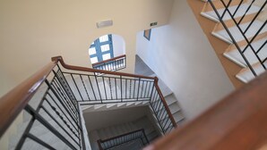 Una escalera con barandilla de madera y balaustradas de metal, que conduce a un rellano con un ventanal de marco azul.