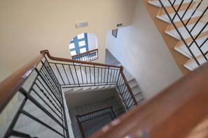 Eine Treppe mit hölzernem Geländer und Metallspindeln, die zu einem Zwischenpodest mit einem blau gerahmten Fenster führt.
