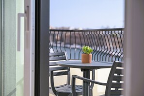 Un balcon avec une table ronde et des chaises, un pot de fleurs et une vue sur le paysage urbain.