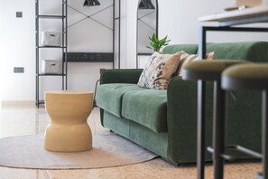 Un salon moderne avec un canapé vert, un pouf beige et une table basse.
