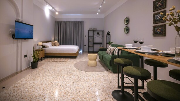 Una habitación de hotel moderna con una cama, un televisor, una mesa de comedor con sillas y un sofá.