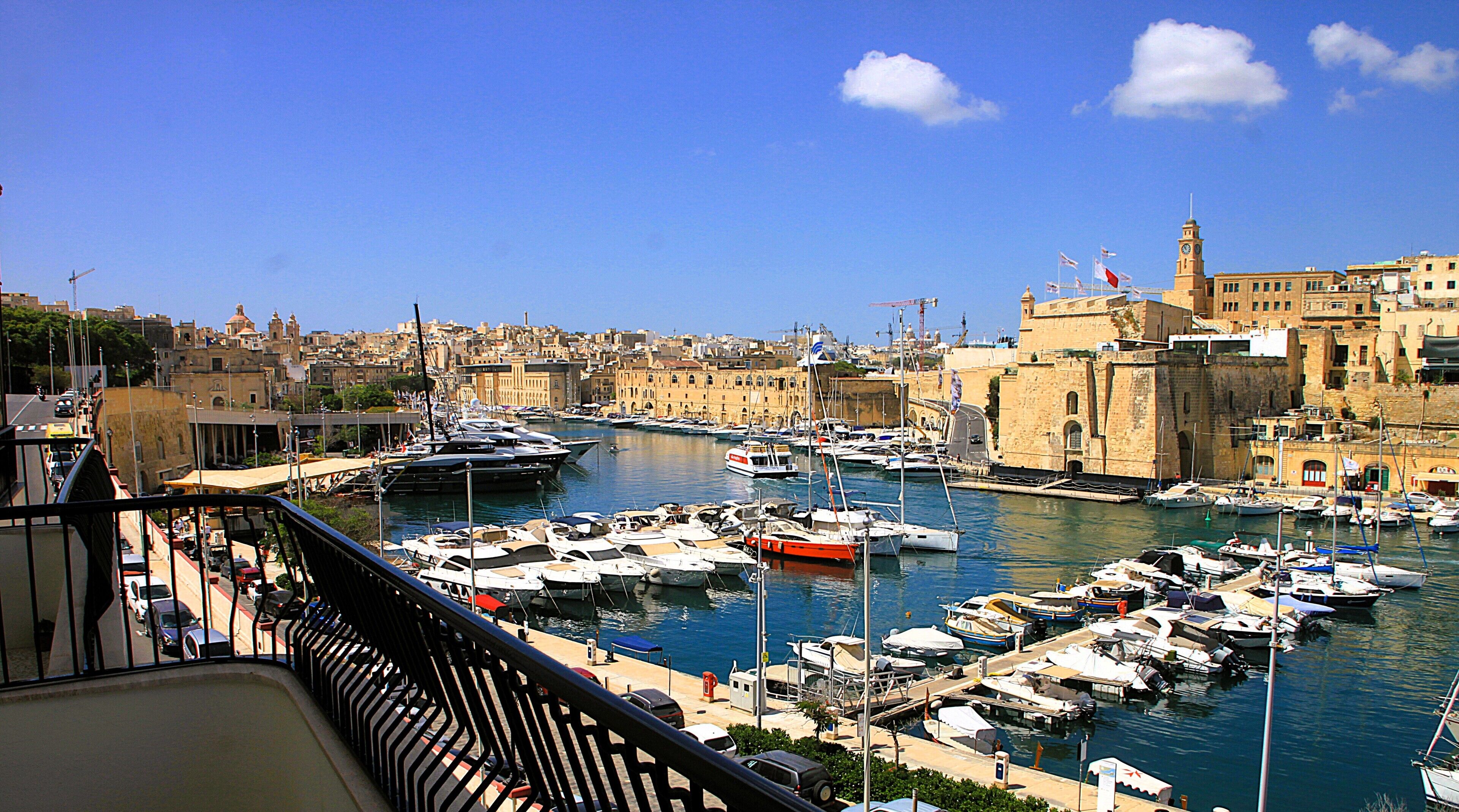 Un puerto deportivo con barcos amarrados, una torre del reloj y edificios históricos al fondo.