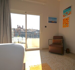 A hotel room with a large sliding glass door, a brown chair, and two paintings on the wall. - SIX • Birgu - 3-bed 3-bath luxury Marina Residence - Valletta ferry (Birgu)
