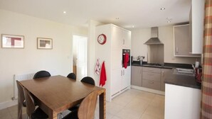 A modern kitchen with a dining area, white walls, and a clock.
