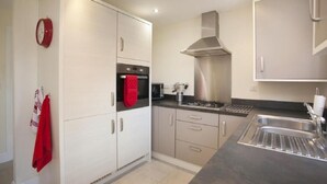 A modern kitchen with white cabinets, a stainless steel range hood, a built-in oven, and a sink.