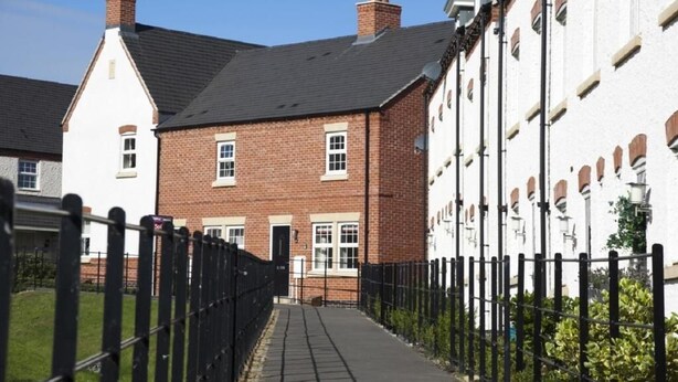 A narrow pathway leading to a brick house with a black roof and white window frames.
