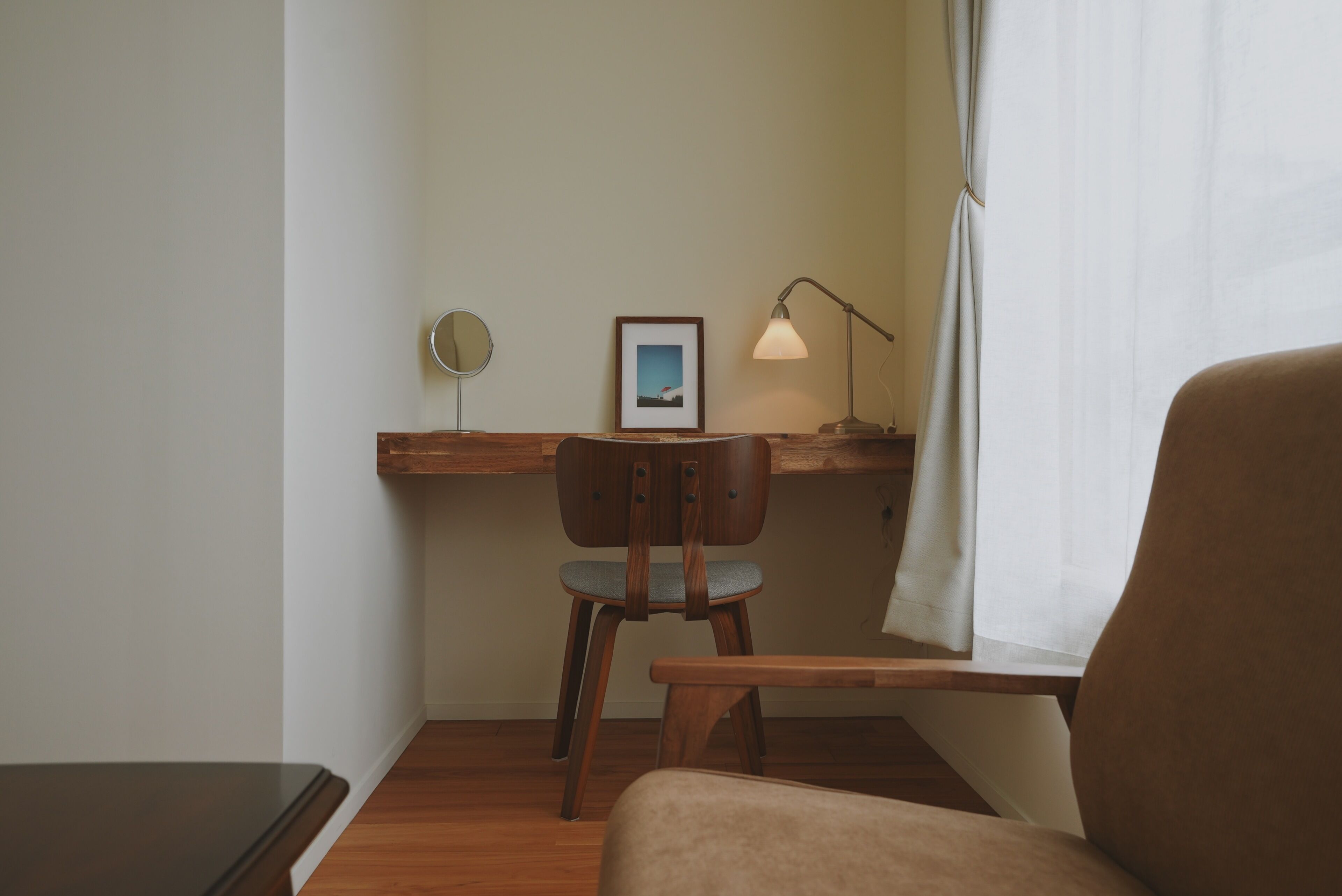 A room with a wooden desk, a chair, a lamp, and a framed picture on the wall.