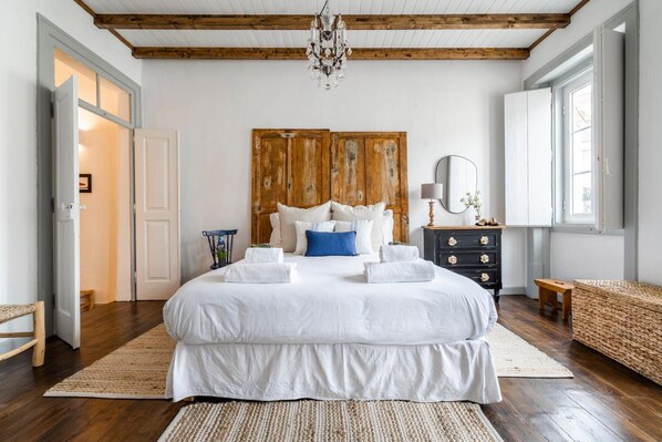 A bedroom with a large bed, wooden headboard, a chandelier, a dresser, and a window.