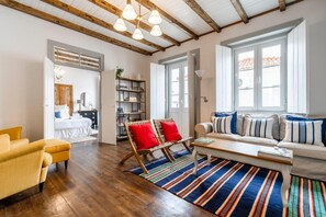 A spacious living room with a wooden floor, a sofa set, a coffee table, and a bookshelf.