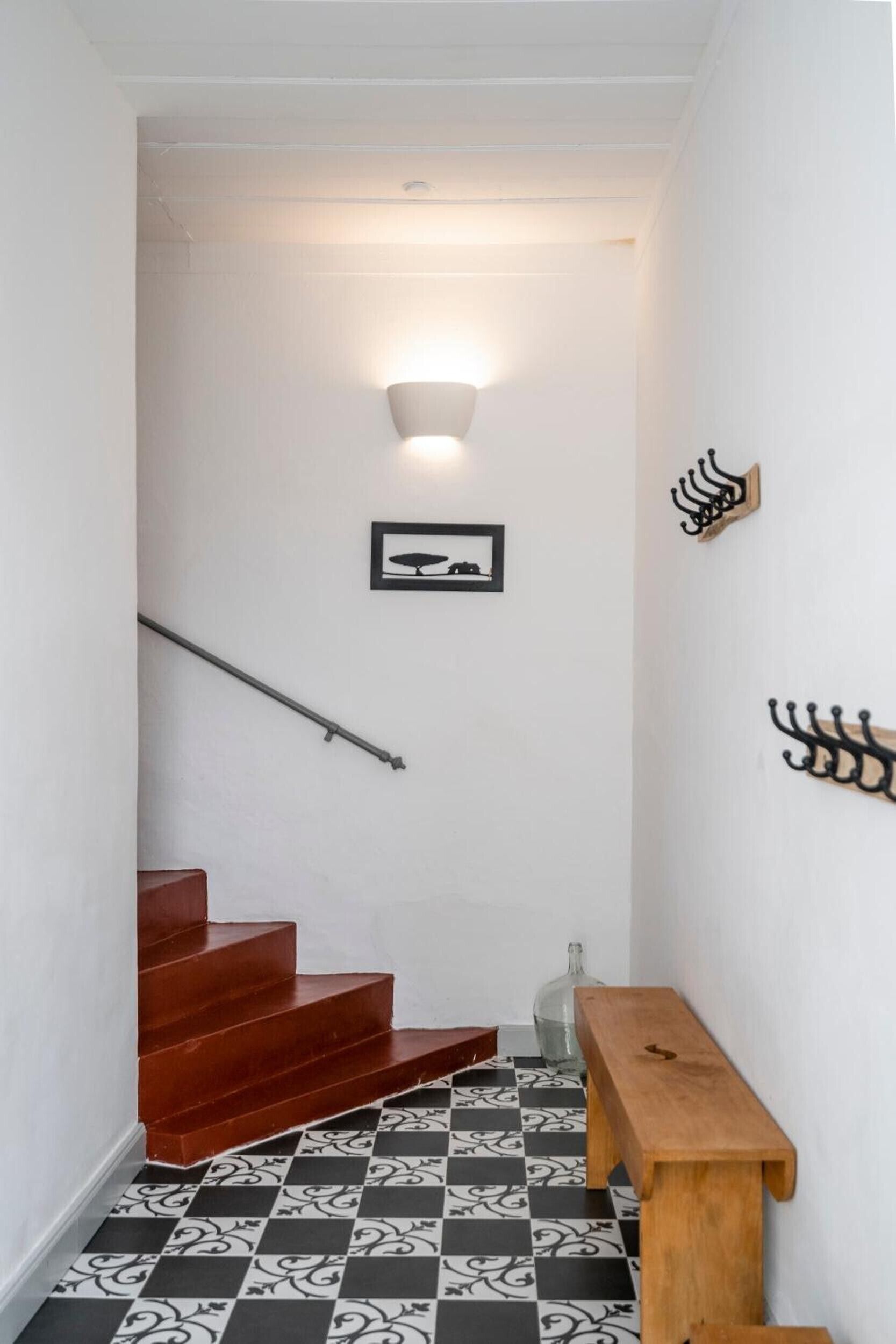 A staircase with a checkered floor, a wooden bench, and a wall-mounted light fixture.
