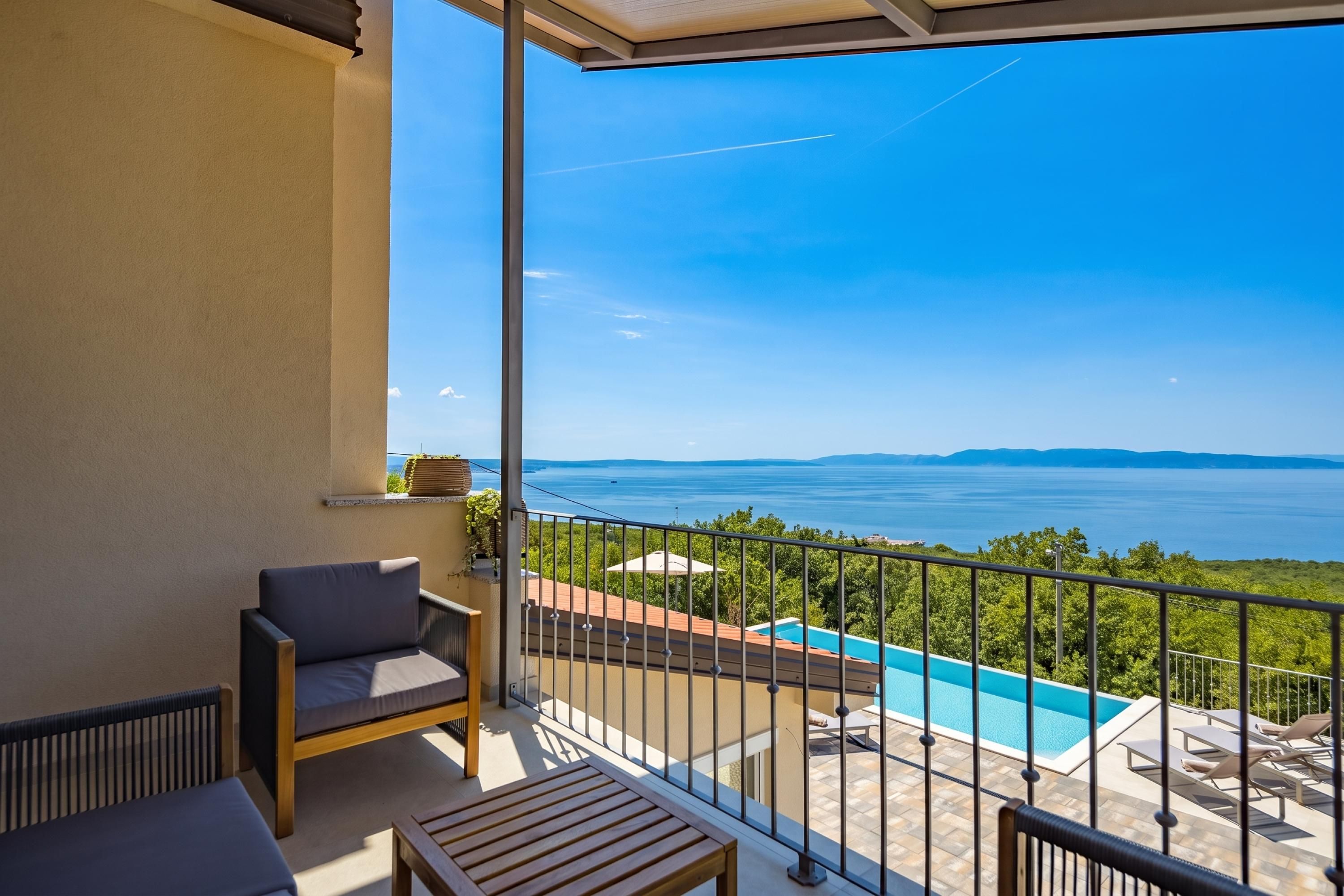 Un balcón con vista al mar, una piscina y una zona de estar.