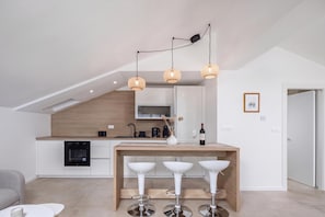 Eine moderne Küche mit Essbereich, inklusive Holztisch mit Barhocker, Pendelleuchten und eingebautem Backofen.