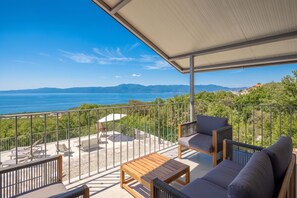 Ein Balkon mit Blick auf das Meer und die Berge, ausgestattet mit einer Couch, Stühlen und einem Tisch.
