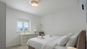 A bedroom with a bed, a nightstand, a window with a view, and a ceiling light. - Holiday Home Elora Seaview Private Pool And Garden (Kostrena)