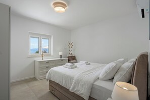 Ein Schlafzimmer mit Bett, Nachttisch, Fenster mit Blick und Deckenleuchte.