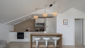A modern kitchen with a dining area featuring a wooden table and three white bar stools. - Holiday Home Elora Seaview Private Pool And Garden (Kostrena)
