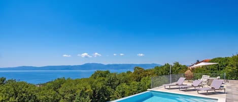 A swimming pool with lounge chairs and a view of the sea and mountains.