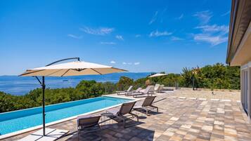 A poolside area with a view of the sea, lounge chairs, and umbrellas.