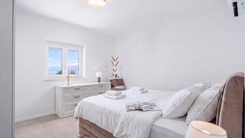 A bedroom with a bed, a window, a dresser, and a bedside table with a lamp.