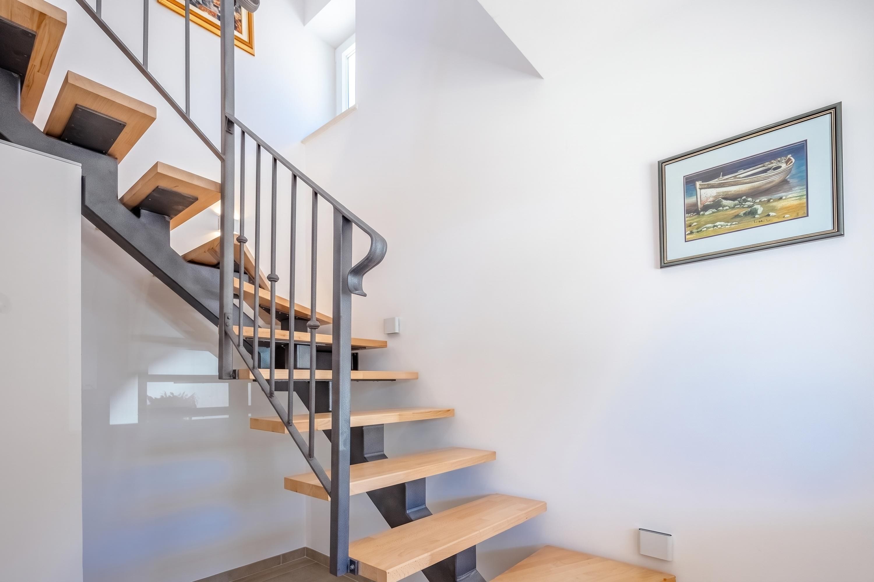 A modern staircase with wooden steps and metal railings, leading to a landing with a framed artwork.