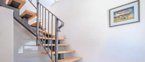 A modern staircase with wooden steps and metal railings, leading to a landing with a framed artwork.