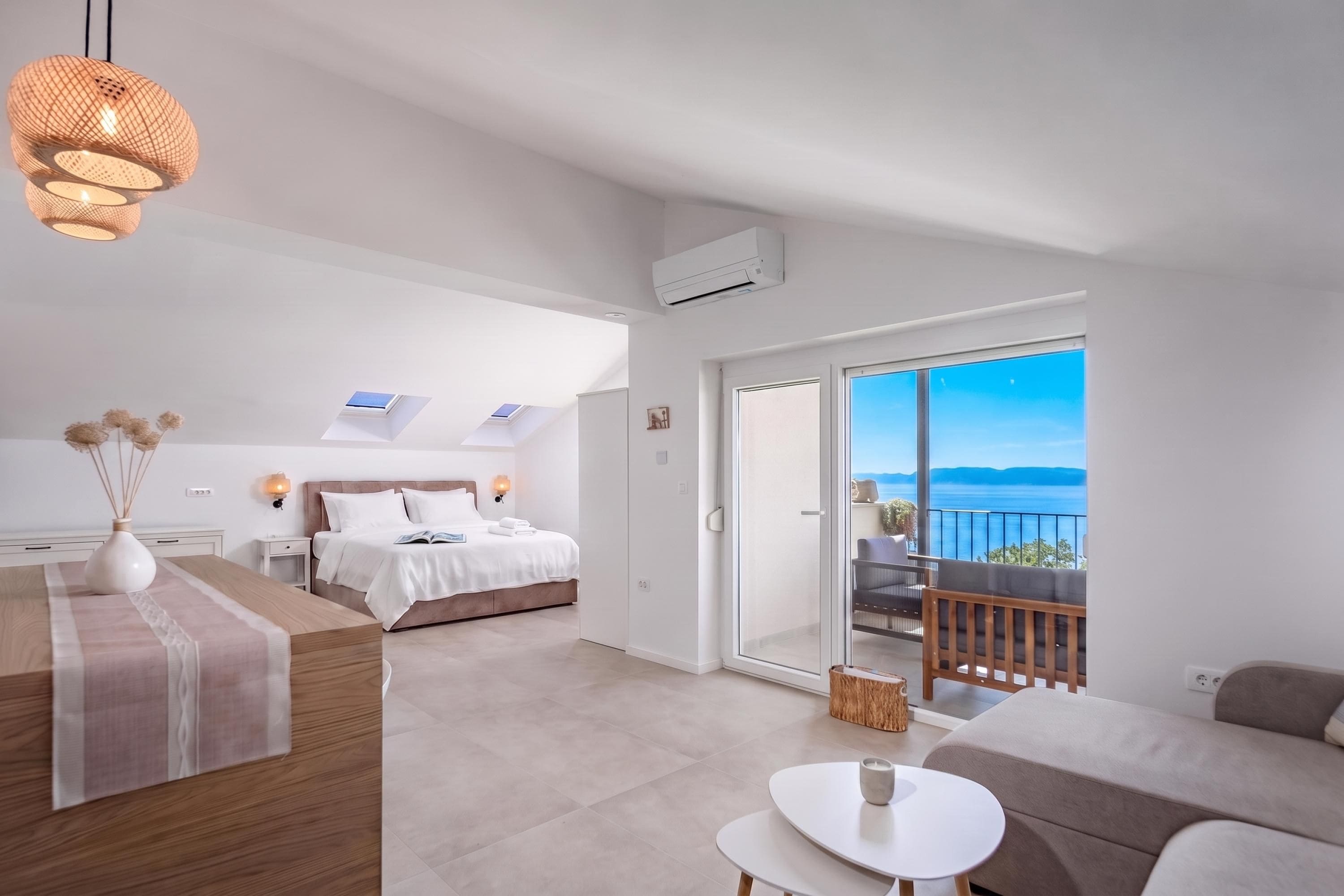 A modern bedroom with a bed, bedside table, and a view of the sea through a balcony.