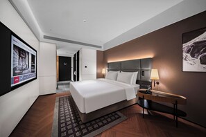 A hotel room with a large bed, a bedside table with a lamp, a wall-mounted TV, and a painting.