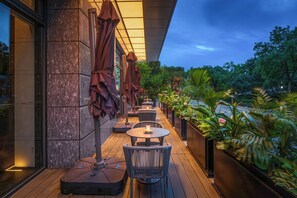 An outdoor seating area with tables and chairs, umbrellas, and potted plants.