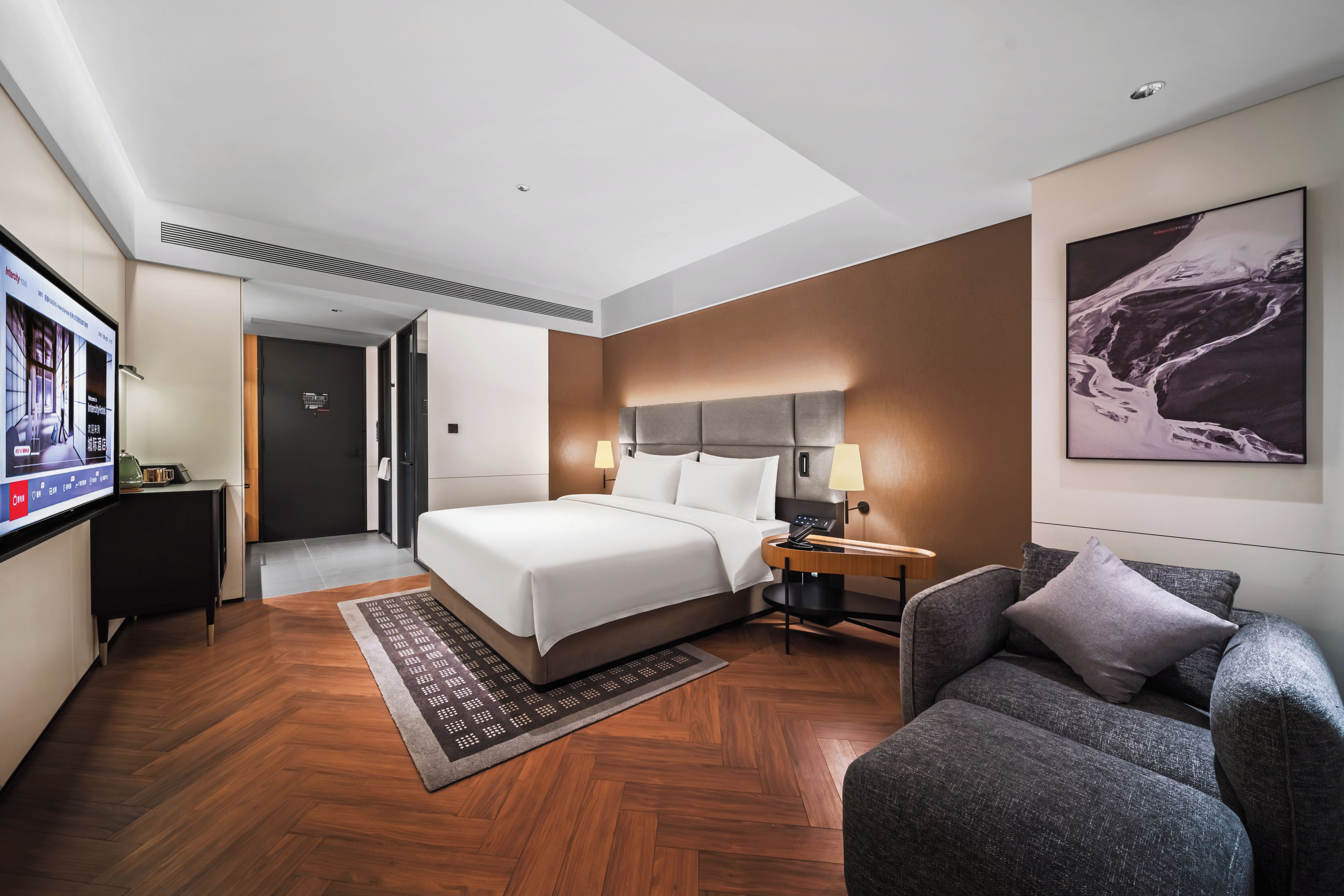 A modern hotel room with a large bed, a desk, a chair, and a television.