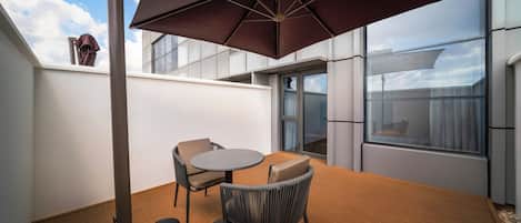 A rooftop terrace with a table and chairs, a large umbrella, and a view of the sky.