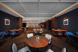 A modern interior with round tables and chairs, a bar area with shelves, and framed pictures on the walls. - Shanghai Intercity Expo Center Hotel (Shanghai)