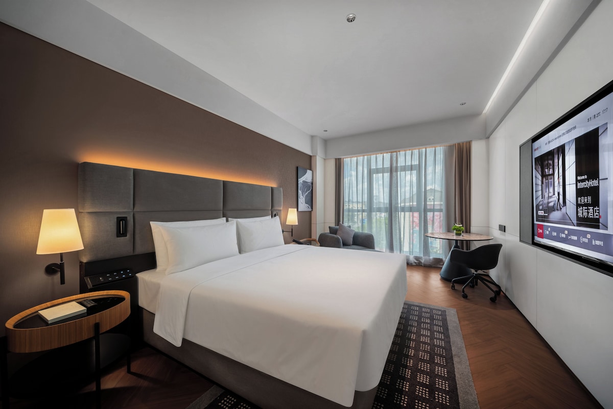 A modern hotel room with a large bed, bedside lamps, a desk, and a television screen displaying a welcome message.