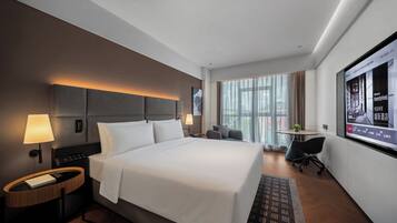 A modern hotel room with a large bed, bedside lamps, a desk, and a television screen displaying a welcome message.