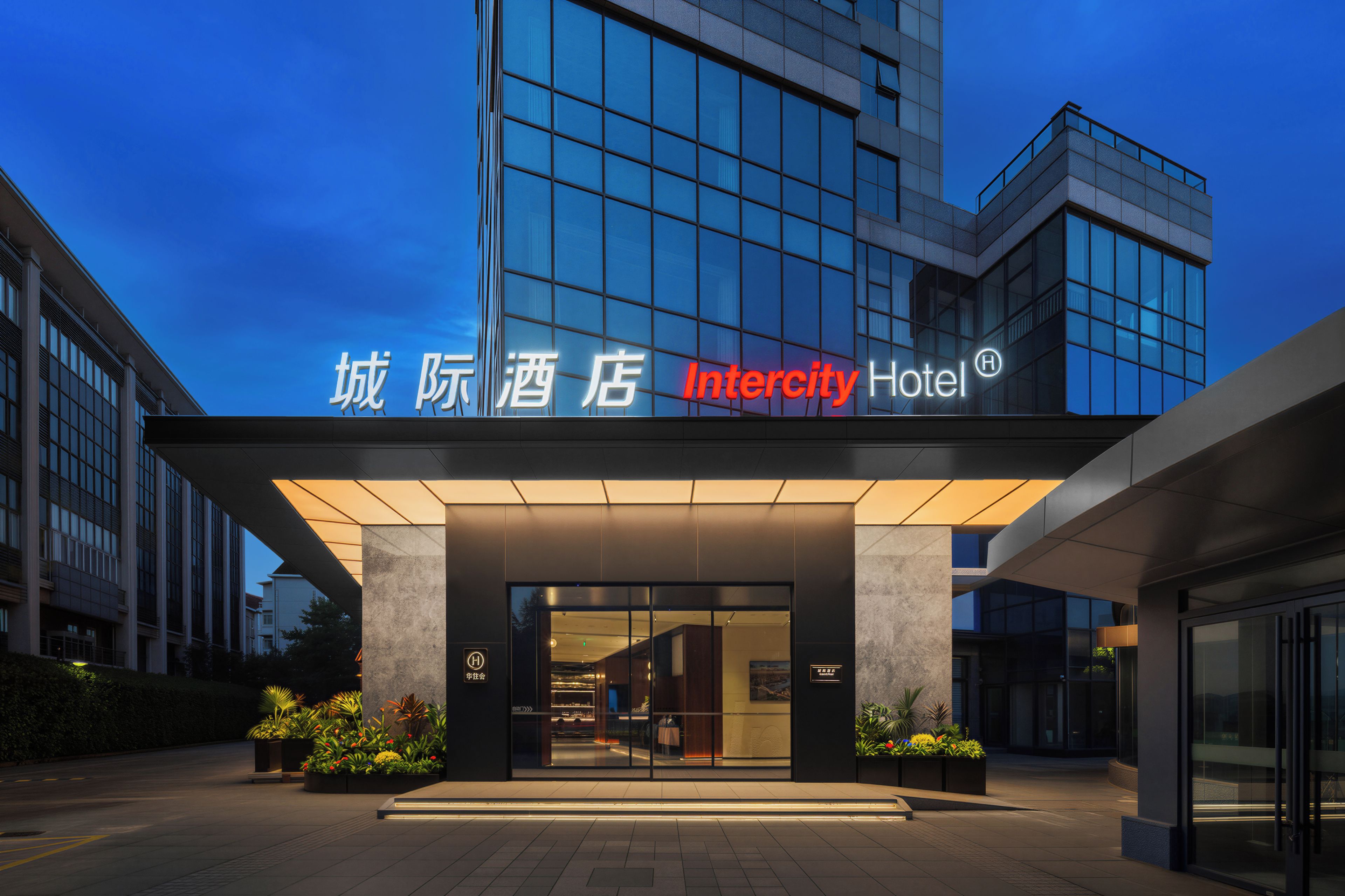 Ein moderner Hotel Eingang mit Glasfassade und beleuchteter Beschilderung.