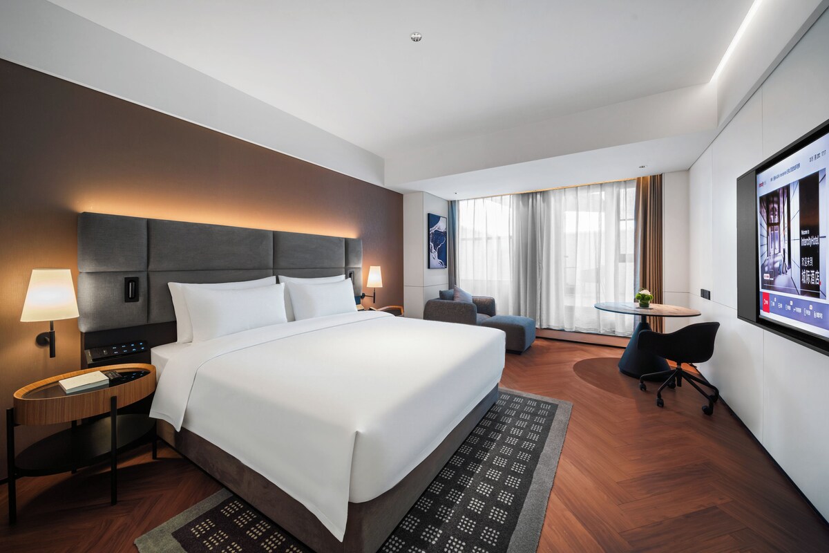 A hotel room with a large bed, bedside tables, a desk, and a chair.