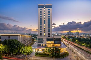 Un hotel moderno con una torre imponente, un ingresso ben illuminato e vista sulla città circostante.