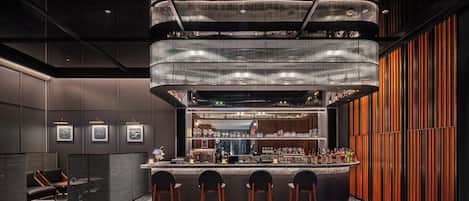 A modern bar area with a central bar counter, multiple seating options, and a distinctive ceiling design.