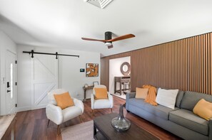 A modern living room with a grey sofa, white armchairs, a wooden accent wall, a ceiling fan, and a sliding door. - Spacious 4-bedroom house in adorable Cincinnati close to downtown (Cincinnati)