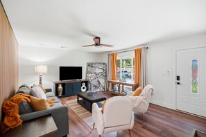 Una sala de estar con sofá, sillón, mesa de centro, televisor y ventilador de techo.