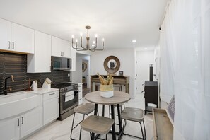 A modern kitchen with white cabinets, a central island with stools, a chandelier, and a round mirror on the wall. - Spacious 4-bedroom house in adorable Cincinnati close to downtown (Cincinnati)