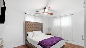 Una camera da letto con un letto grande, una ventola a soffitto, un comodino con una lampada e una finestra con tende.