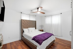 A bedroom with a large bed, a ceiling fan, a bedside table with a lamp, and a window with curtains. - Spacious 4-bedroom house in adorable Cincinnati close to downtown (Cincinnati)