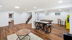 Un'ampia stanza con pavimento in legno, tavolo da biliardo, bicicletta e una scala che conduce in un'altra zona.