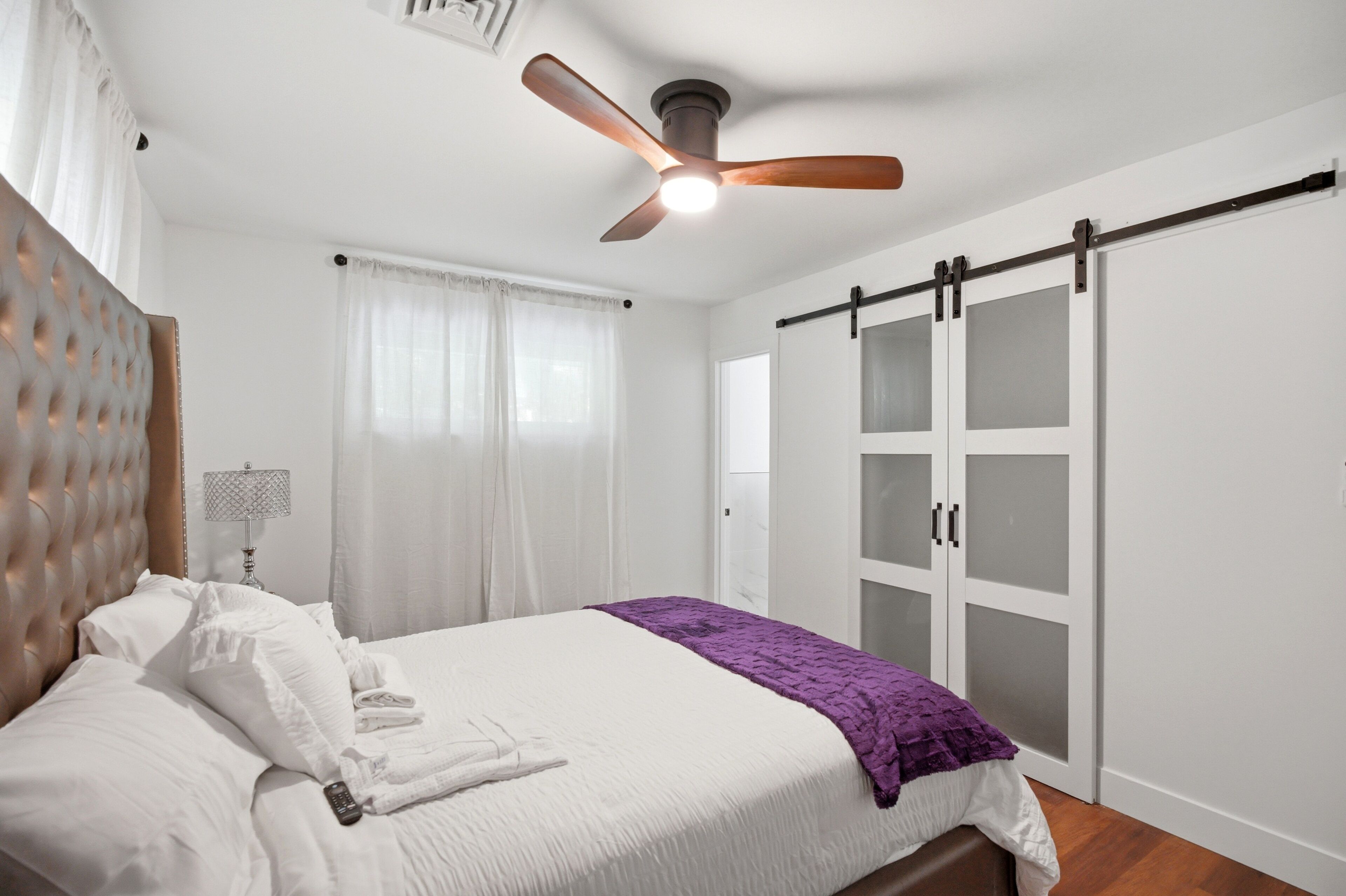 A bedroom with a bed, a ceiling fan, a wardrobe, and a window with curtains.