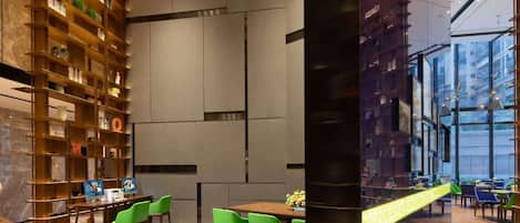 Un interior moderno con una amplia estantería, un comedor con sillas verdes y vistas a través de un muro de cristal.