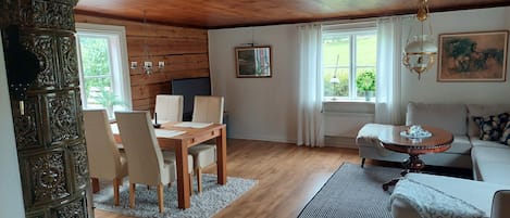A cozy room with a wooden ceiling, a dining table with chairs, a sofa, and a small table with a lamp.