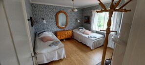 Ein Schlafzimmer mit zwei Betten, einem Schminktisch, einem Spiegel und einem Fenster mit Blick ins Grüne.