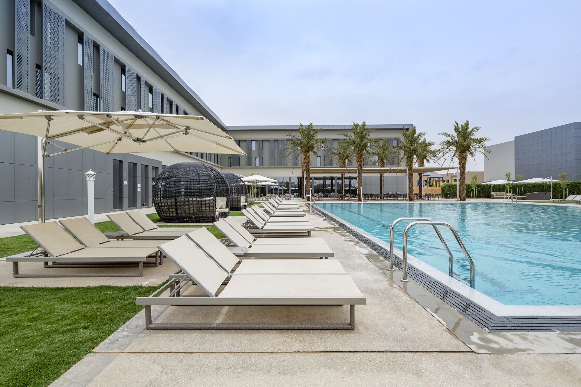 Un área junto a la piscina con sillones de descanso, sombrillas y palmeras.
