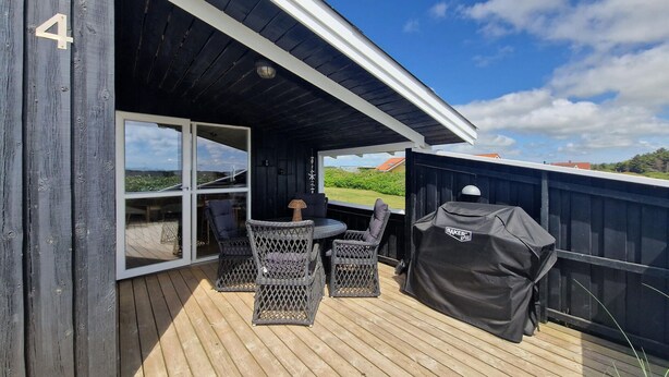 En terrass med möbler i rotting, ett skydd för grillen och utsikt över landskapet.